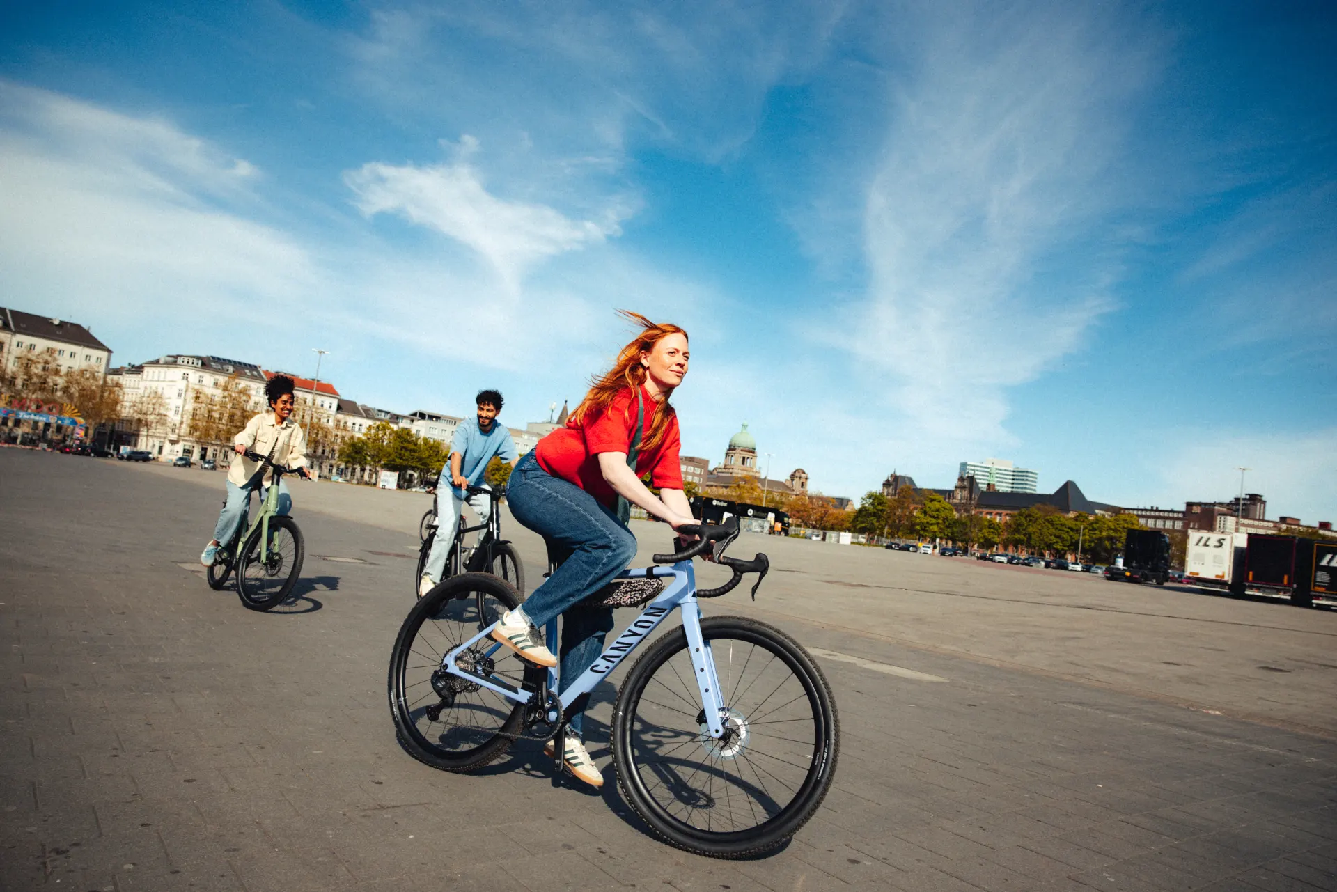 Gruppe junger Menschen radelt auf Leasing Bikes über urbanen Platz, vorne Frau auf Canyon Gravel